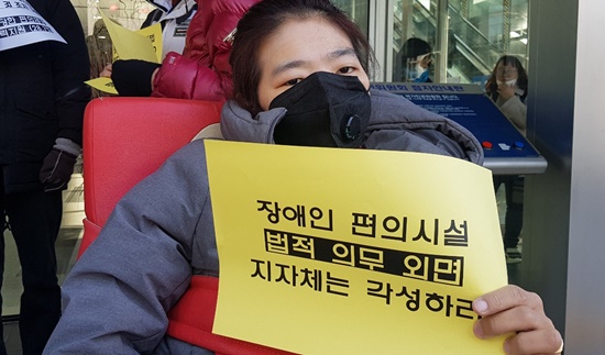 ‘장애인 편의시설 법적 의무 외면 지자체는 각성하라‘ 손피켓을 든 중증장애인.ⓒ에이블뉴스