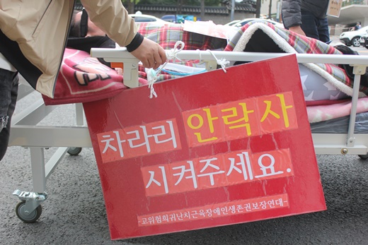 ‘차라리 안락사 시켜주세요’ 피켓이 걸린 침대에 누운 근육장애인 모습.ⓒ에이블뉴스DB

